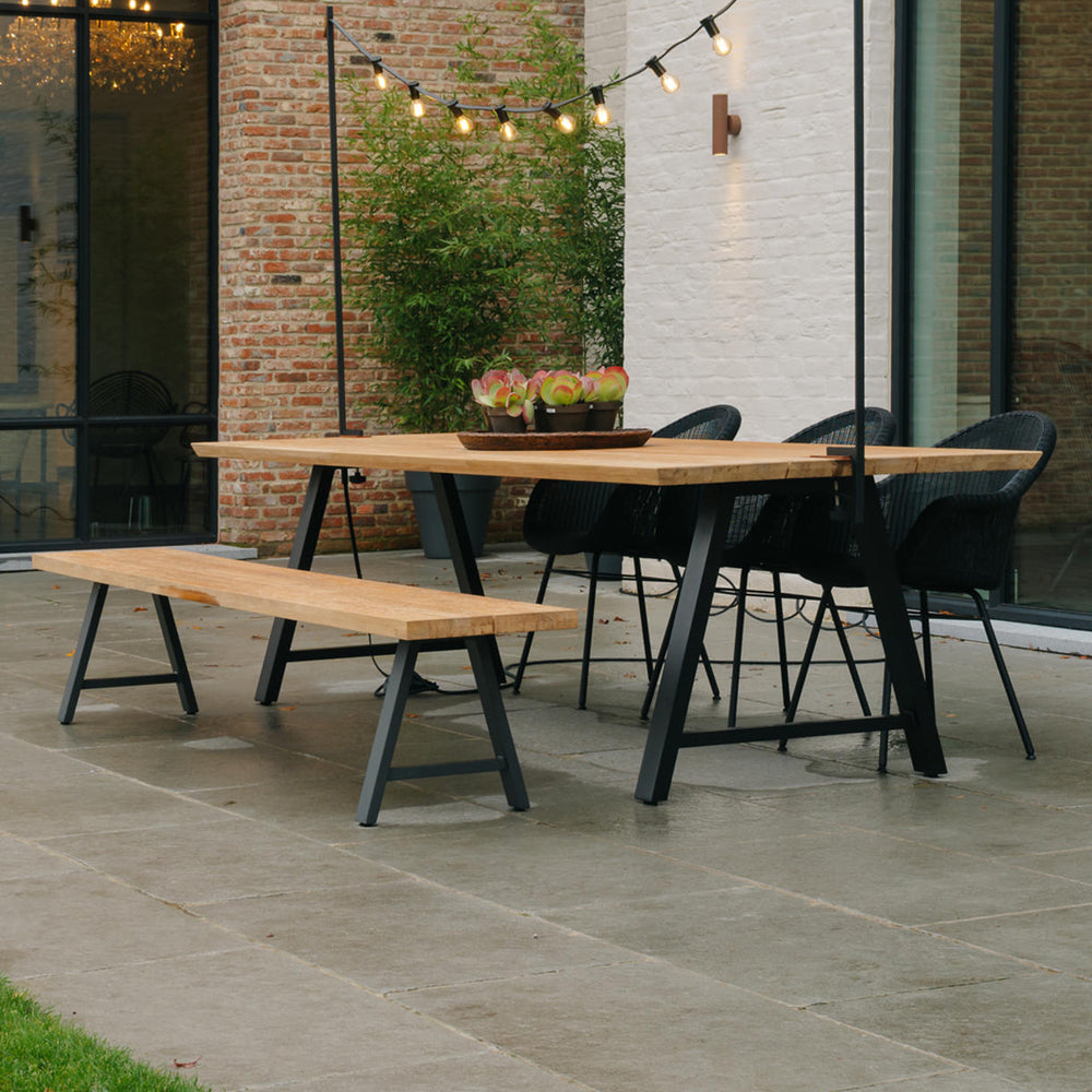 A teak dining bench with matching table sits in a courtyard